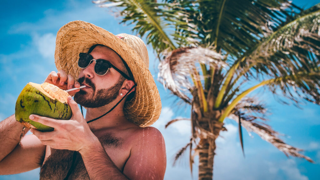 man drinking from a coconut under palm tree