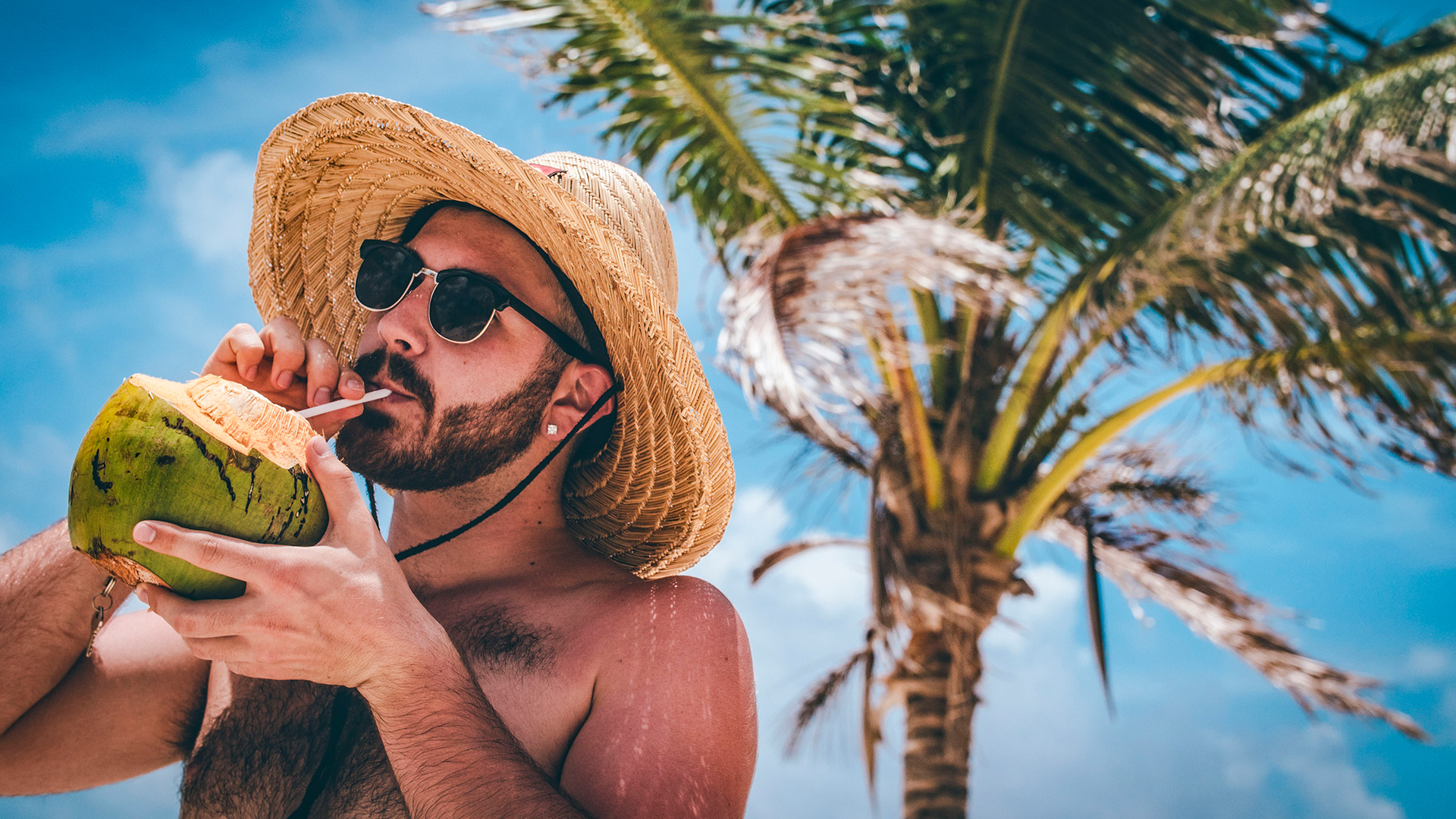 man drinking from a coconut under palm tree